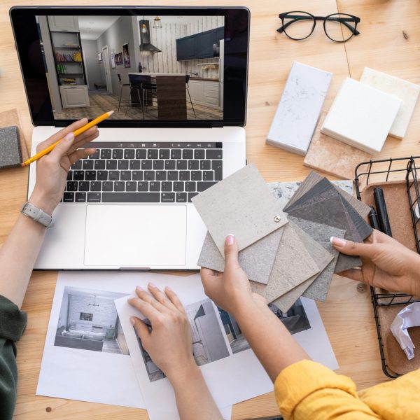 Contemporary designer pointing at home interior example on laptop display while consulting with colleague holding linoleum samples